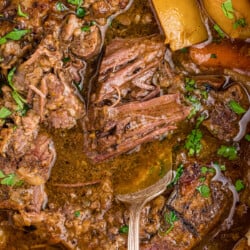 Juicy pot roast recipe on a serving fork in the pot with gravy, potatoes, and carrots.