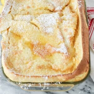 Close up of puffed german pancake in glass baking dish with powdered sugar sprinkled over the top.