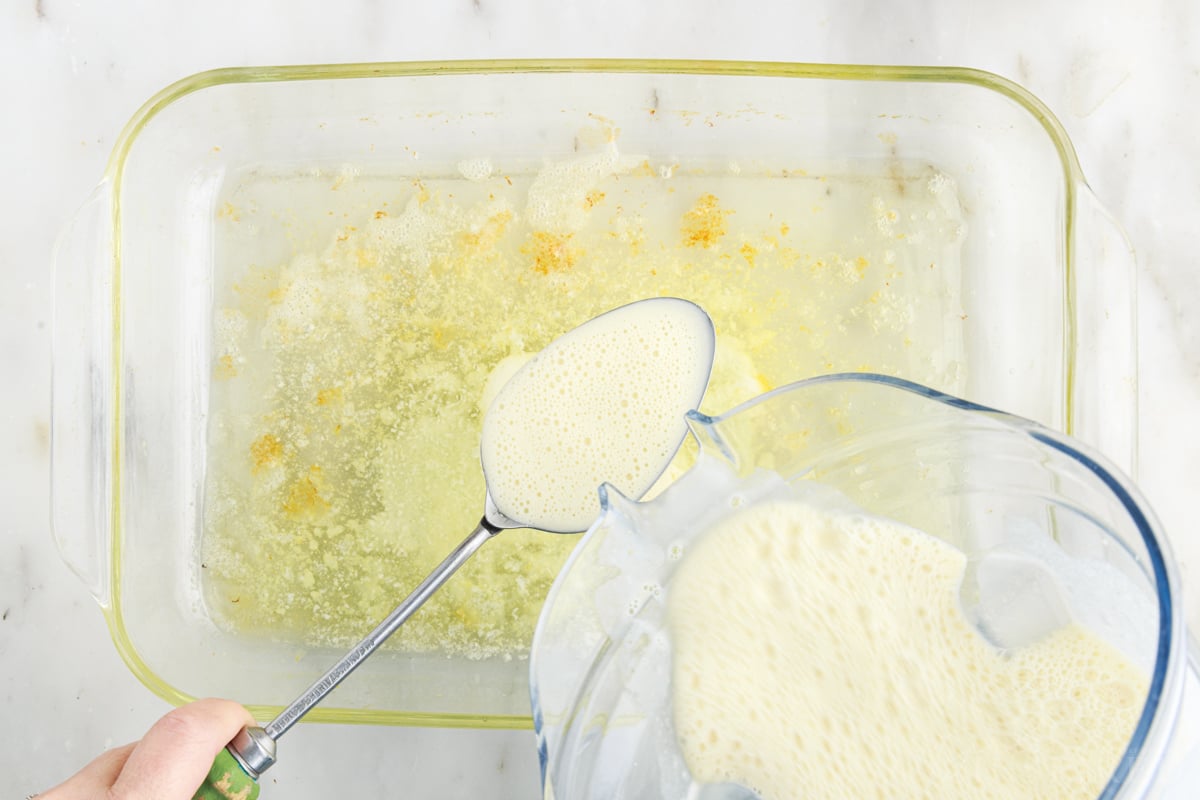 Pouring batter over metal spoon into melted butter in glass baking dish.
