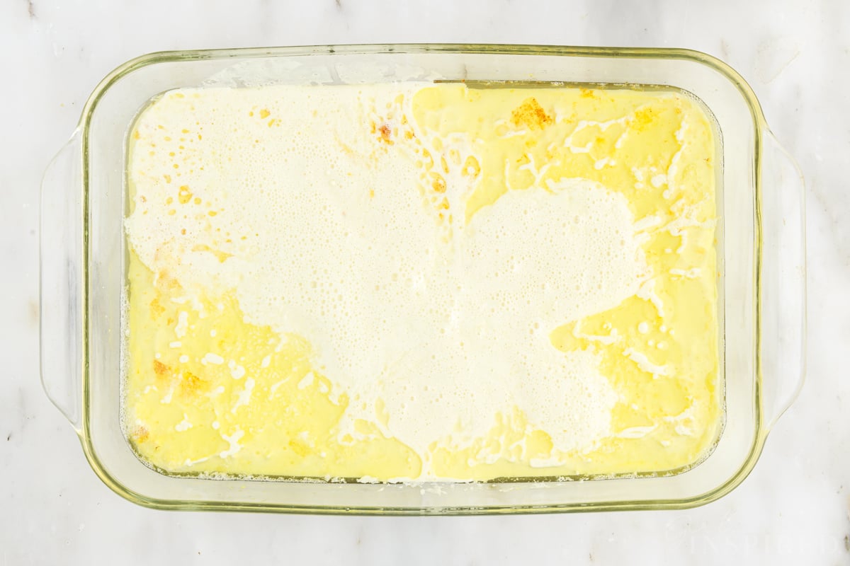 German pancake batter with some butter floating over it in glass baking dish.