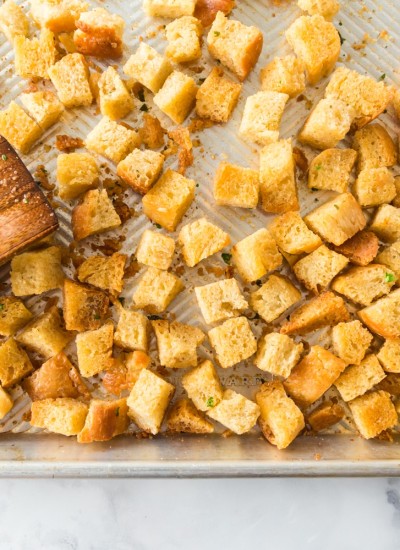 homemade croutons browned and spread out on baking sheet with wooden spatula