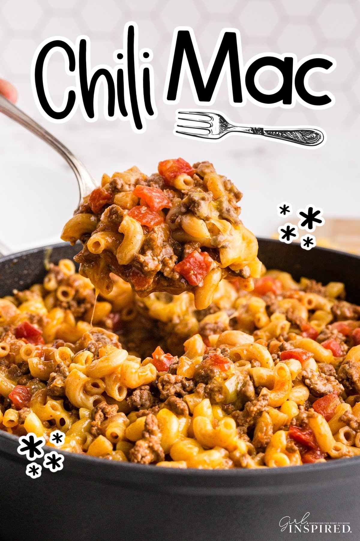 Spoon scooping Chili Mac from saucepan, piled with macaroni noodles, cheese, ground beef, and tomatoes.