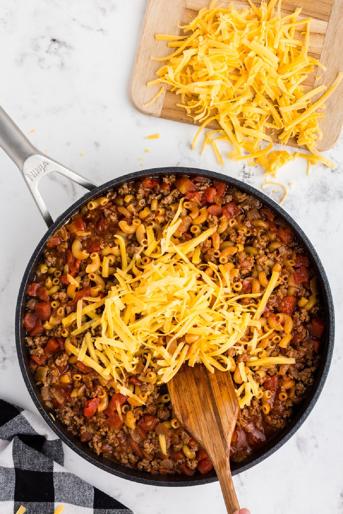 Stirring pile of cheese into the chili mac in skillet.