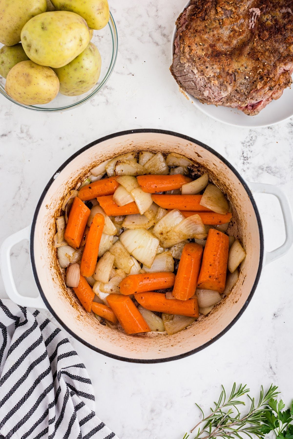 Browned onions and carrots in stock pot with meat and potatoes set to the side.