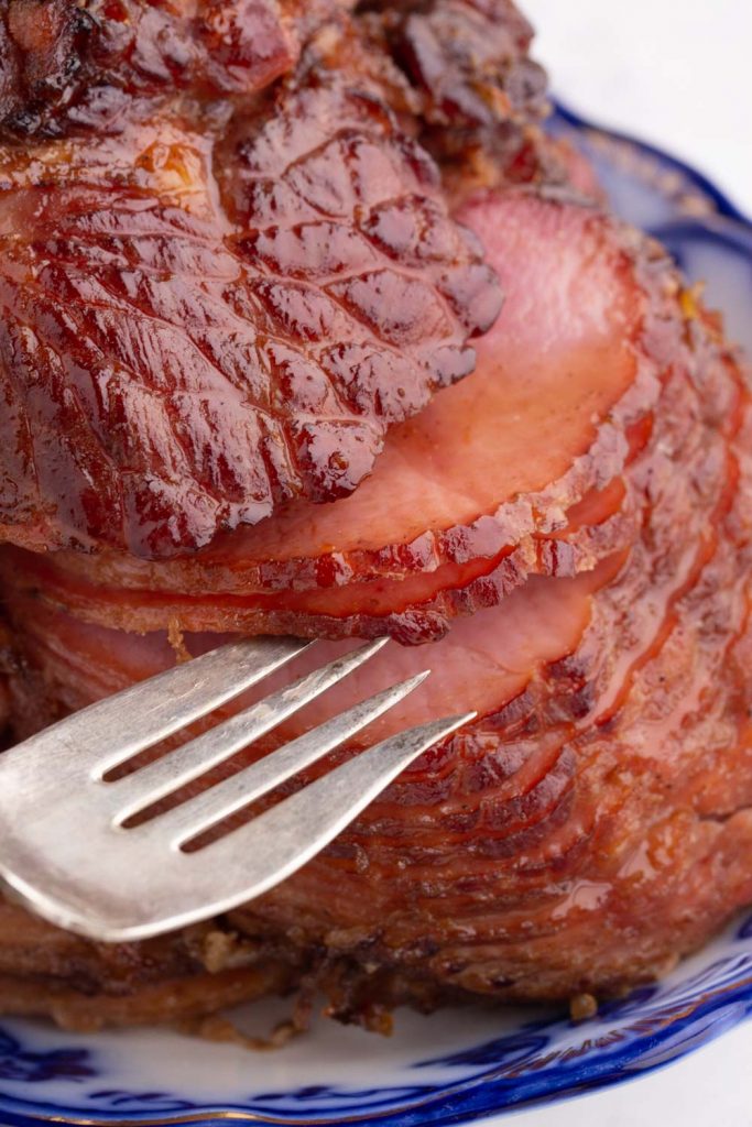 close up of sliced ham on blue platter with fork separating slices