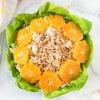 chicken salad in bowl with lettuce bed, orange slices and slivered almonds on top, linen and orange halves on counter