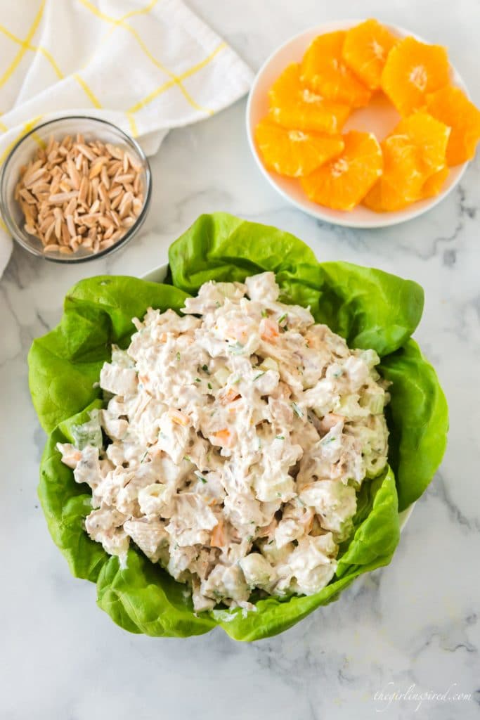 chicken salad mounded in bowl of lettuce leaves with oranges and almonds to the side