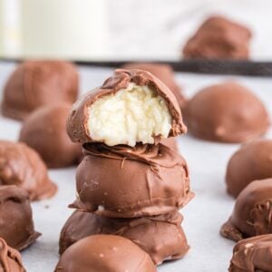 Stack of chocolate coconut balls on a sheet pan of finished balls, with bite taken out of top of stack.