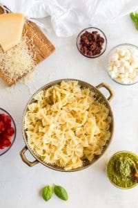 bowtie pasta in colander with pesto, cheese, and tomatoes in nearby bowls