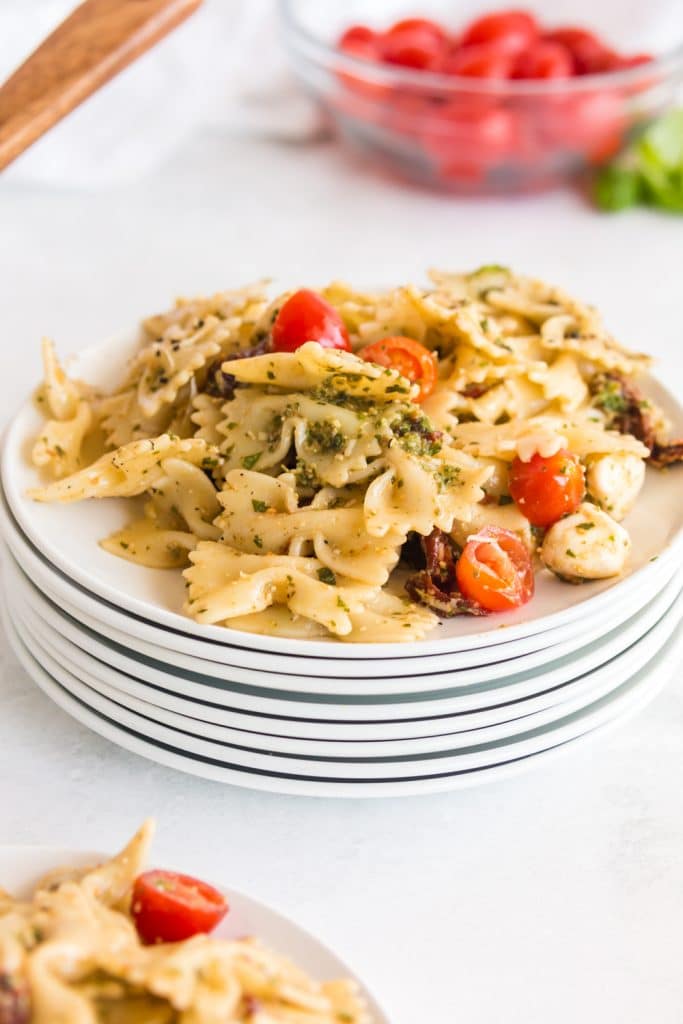 pesto pasta salad piled on a stack of white plates