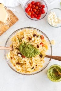 pesto sauce mounded on top of pasta salad in glass salad bowl