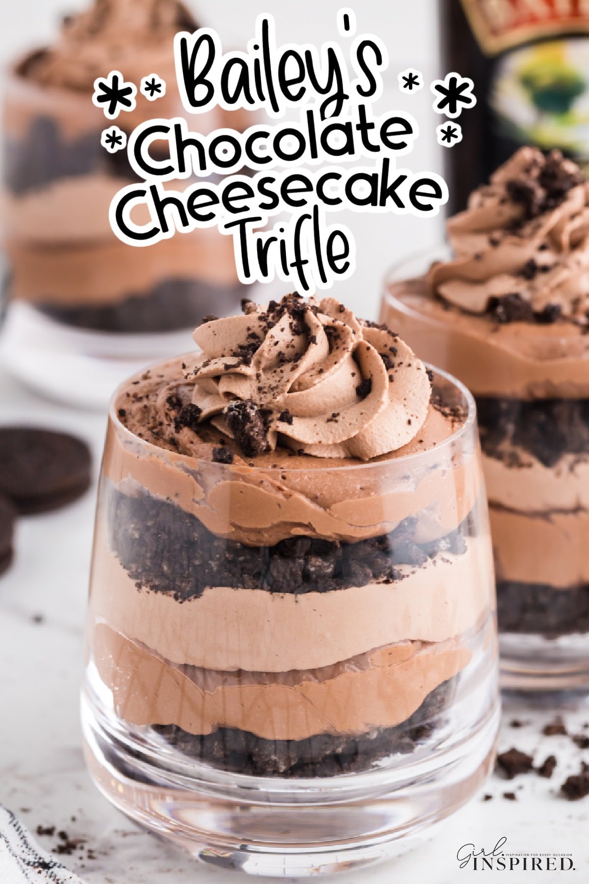 Layered chocolate cheesecake and cookie crumbs in a stemless wine glass and text title "Bailey's Chocolate Cheesecake Trifle."