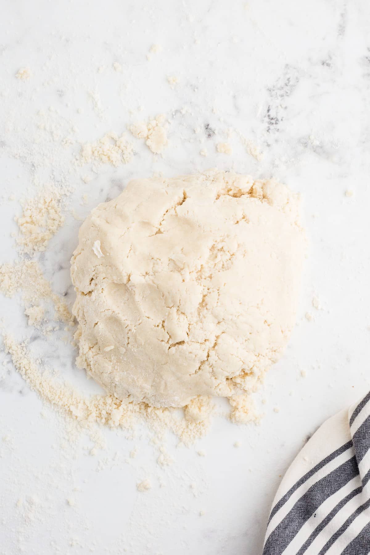 Mound of kneaded Butter Pie Crust dough on marble countertop, grey and white striped linen