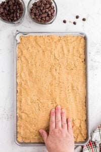 hand pressing peanut butter mixture into jelly roll pan