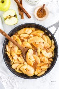 Frying pan with Fried Apples and wooden spoon on marble countertop