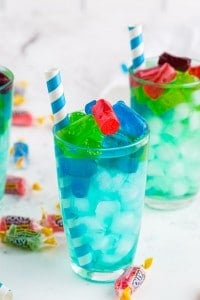 Two glasses of turquoise Jolly Rancher Cocktail with paper straws, jolly rancher candy on marble countertop