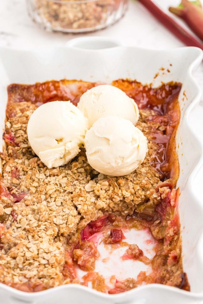 baked Rhubarb Crisp in white pie dish, three scoops of vanilla ice cream on top