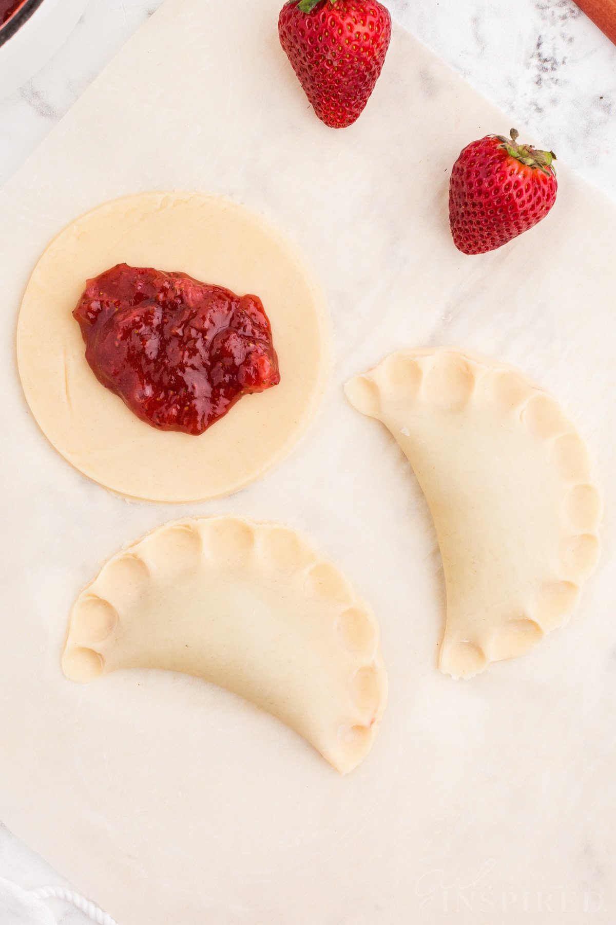 Several strawberry rhubarb hand pies, two are folded into half-moons and sealed along the edges.