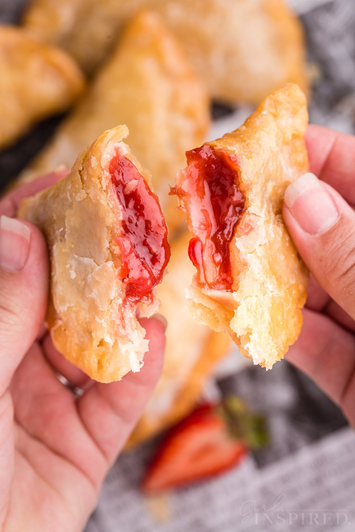 Holding two halves of a strawberry rhubarb hand pie broken open.