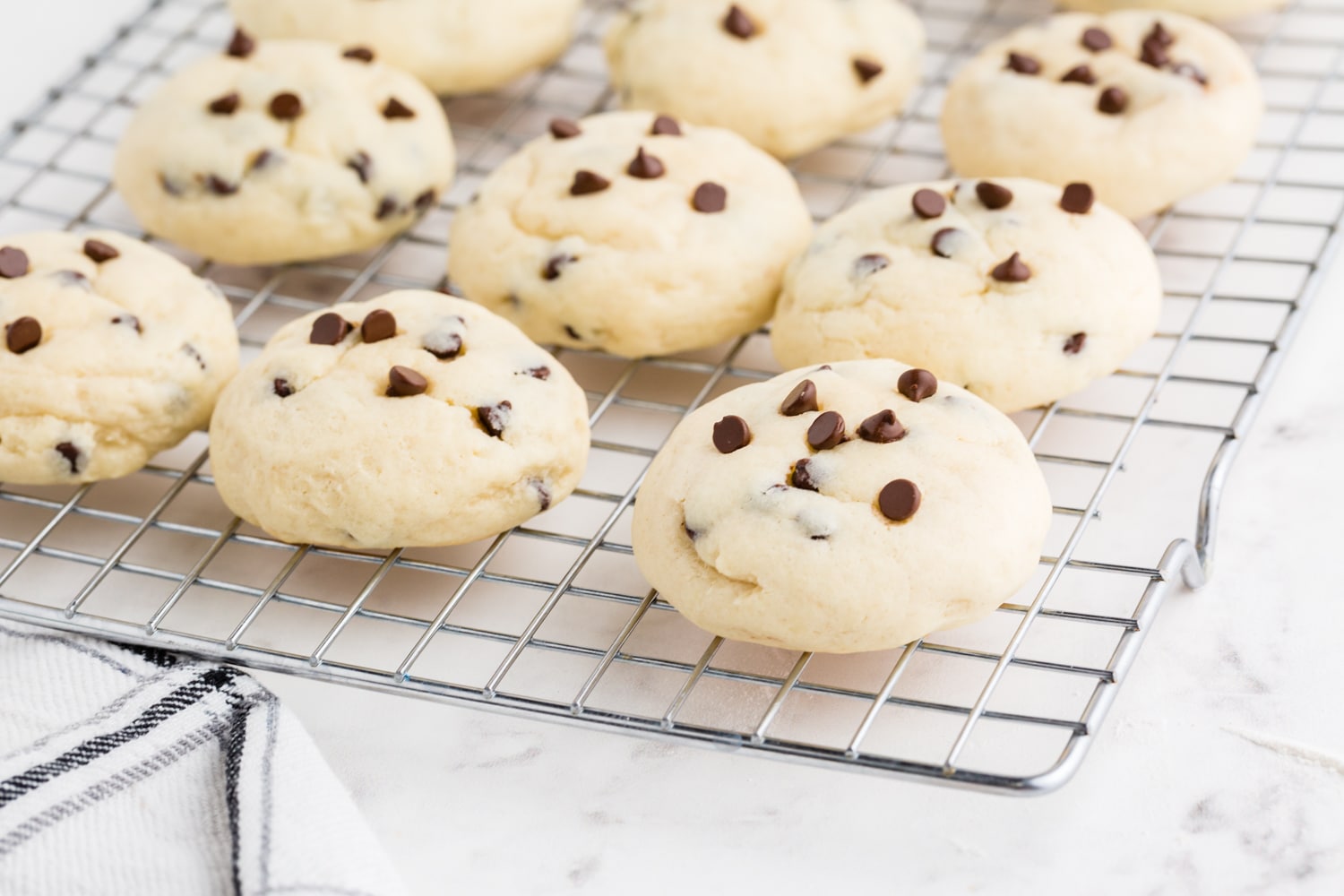Chocolate Chip Cheesecake Cookies on a cooling rack on a marble countertop, striped kitchen linen
