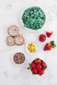 Bowl with green chocolate melts, oatmeal cookies, strawberries, golden star candy, sprinkles, bowl with strawberries on a marble countertop