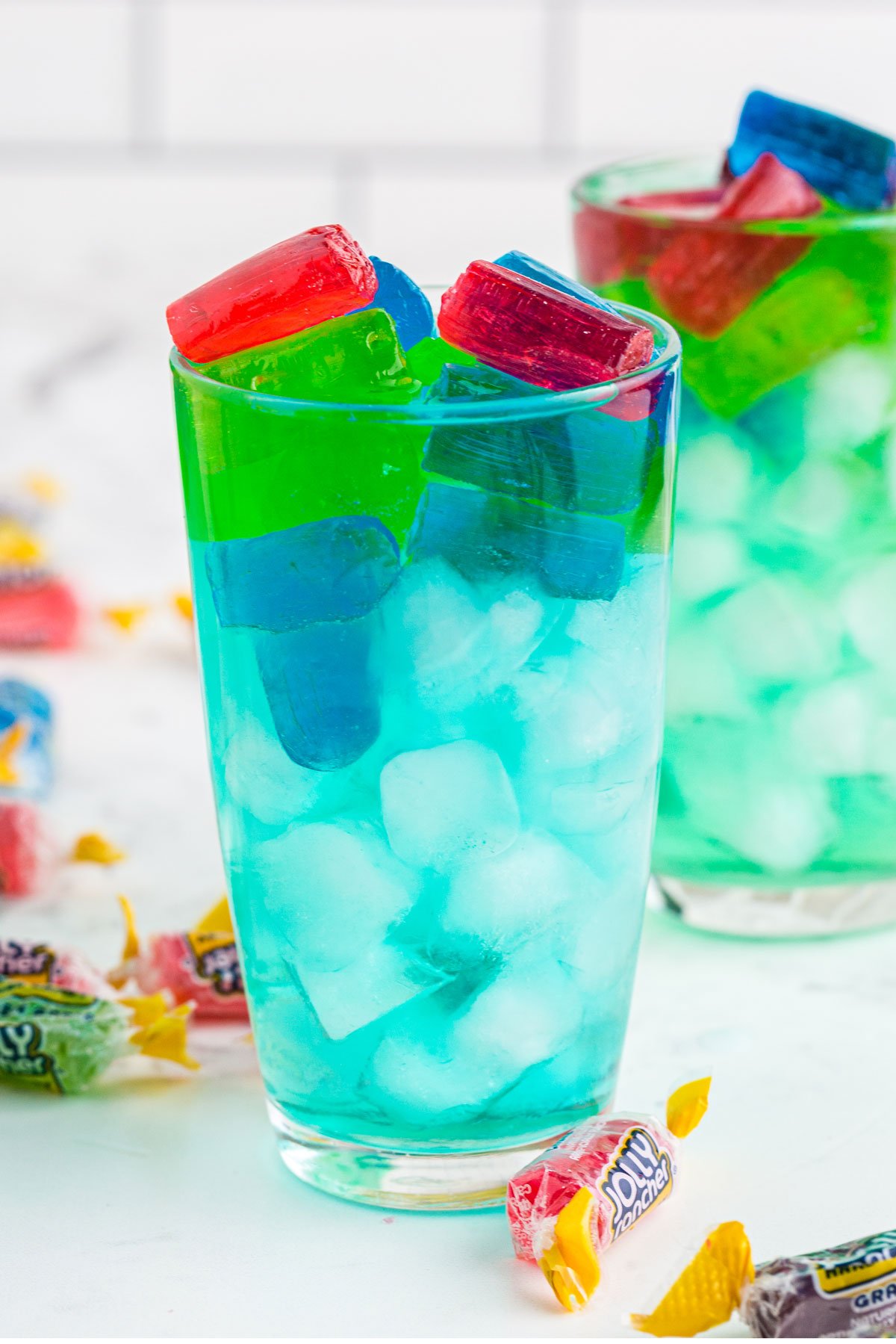 Blue Jolly Rancher cocktail in glass with ice and topped with pile of red, blue and green jolly rancher candies.