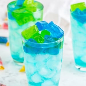 Three glasses of turquoise Jolly Rancher Cocktail with jolly rancher candy on marble countertop.