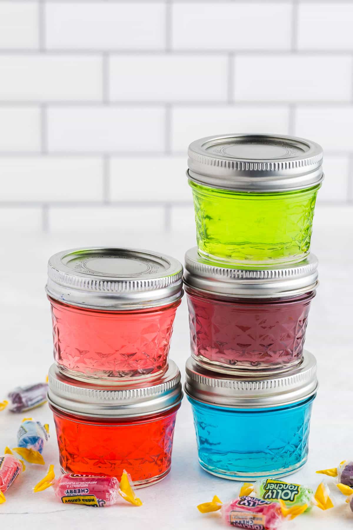 Stacked mason jars of different colored Jolly Rancher vodka.