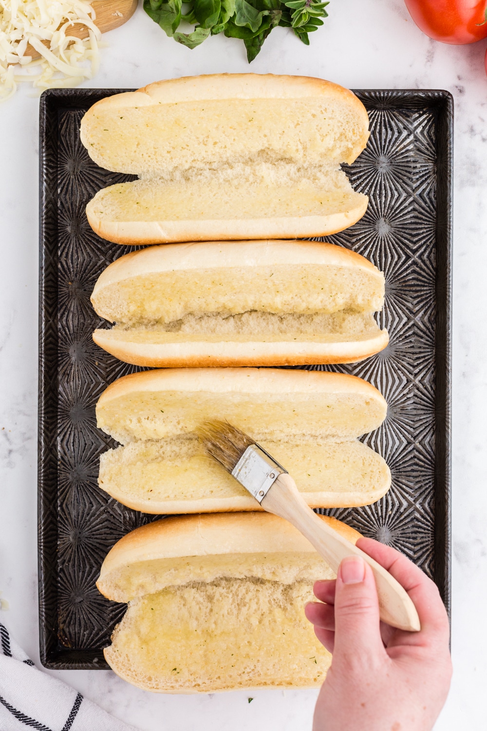 Sandwich buns on cookie sheet being brushed with melted butter.