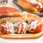 Meatball Sub on a cake plate, bowl of marinara sauce, on a marble countertop