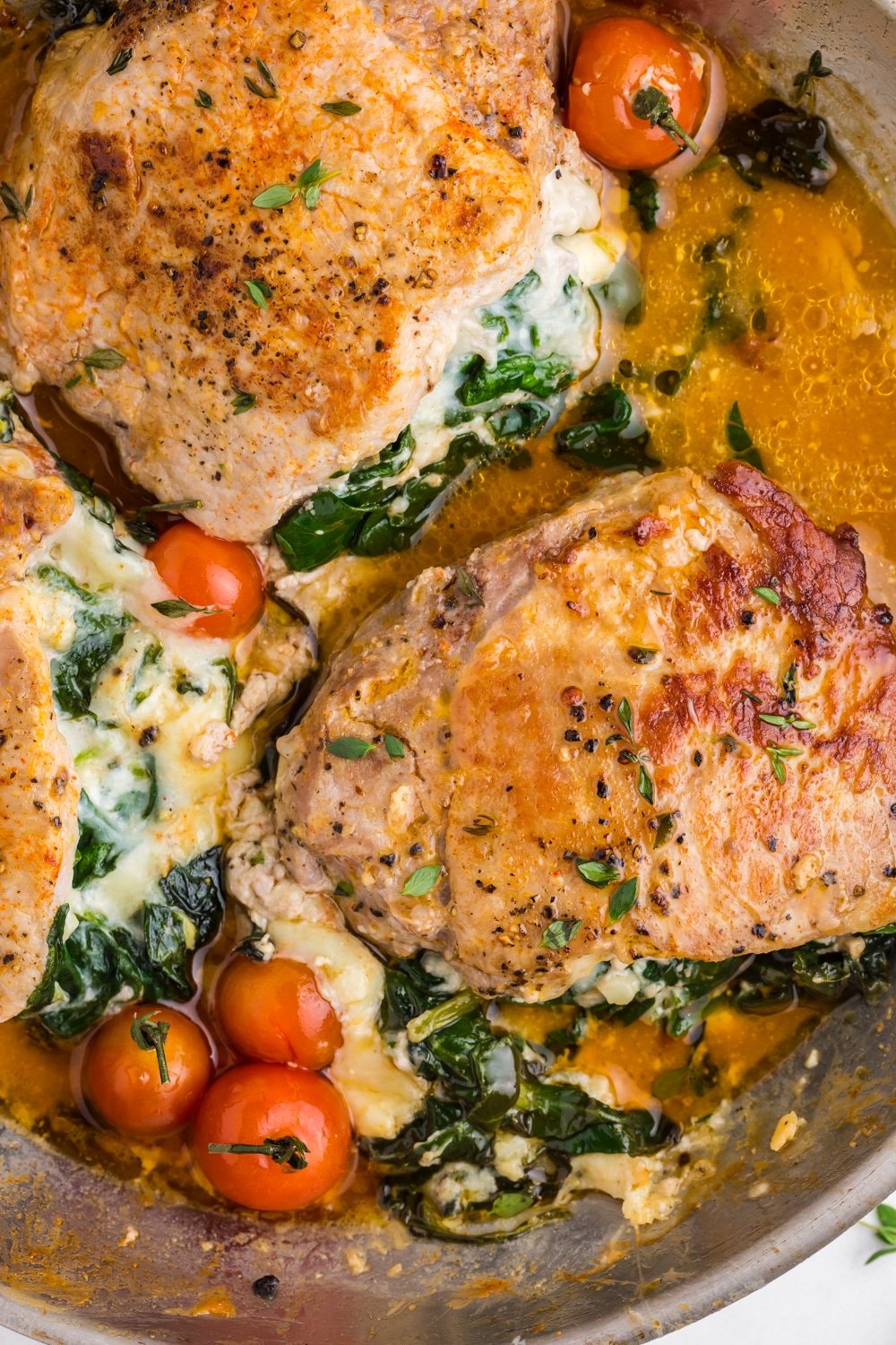 Close up of stuffed pork chops with cherry tomatoes in a skillet.