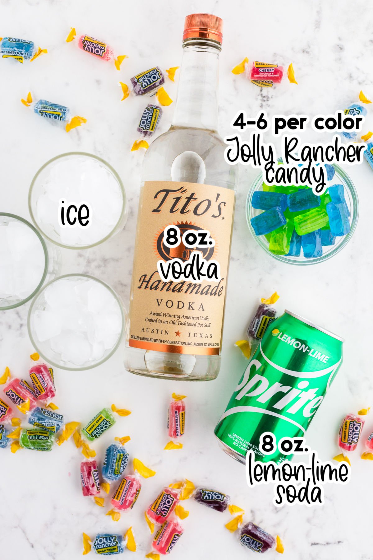 Ingredients for jolly rancher cocktail: 3 glasses filled with ice, a bottle of vodka, lemon soda can, jolly rancher candy on a marble countertop with text labels.