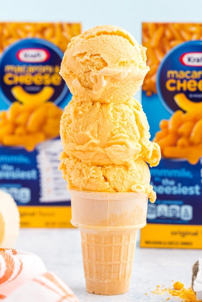 scooped cheese ice cream on a cone with boxes of mac and cheese in background