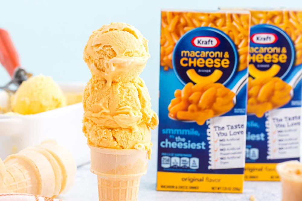 scooped cheese ice cream on a cone with boxes of mac and cheese in background