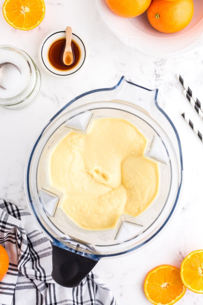 Blender with mixed Orange Julius ingredients on a light countertop black and white kitchen linen paper straws