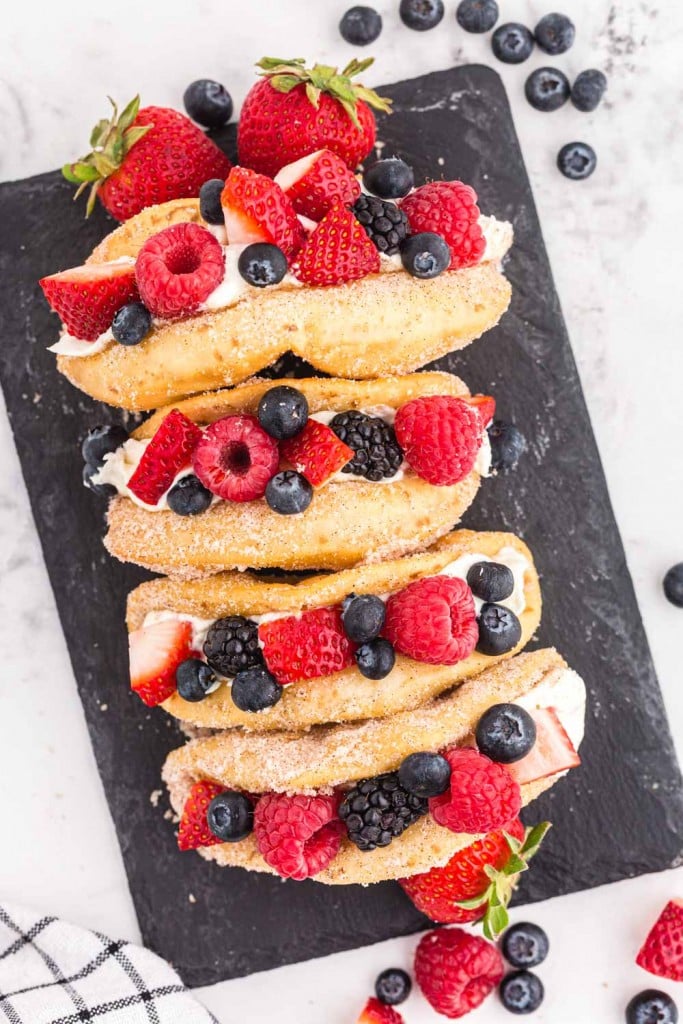Mixed berry cheesecake tacos on a black slate stone tile, fresh berries, black and white checked linen, on a marble countertop