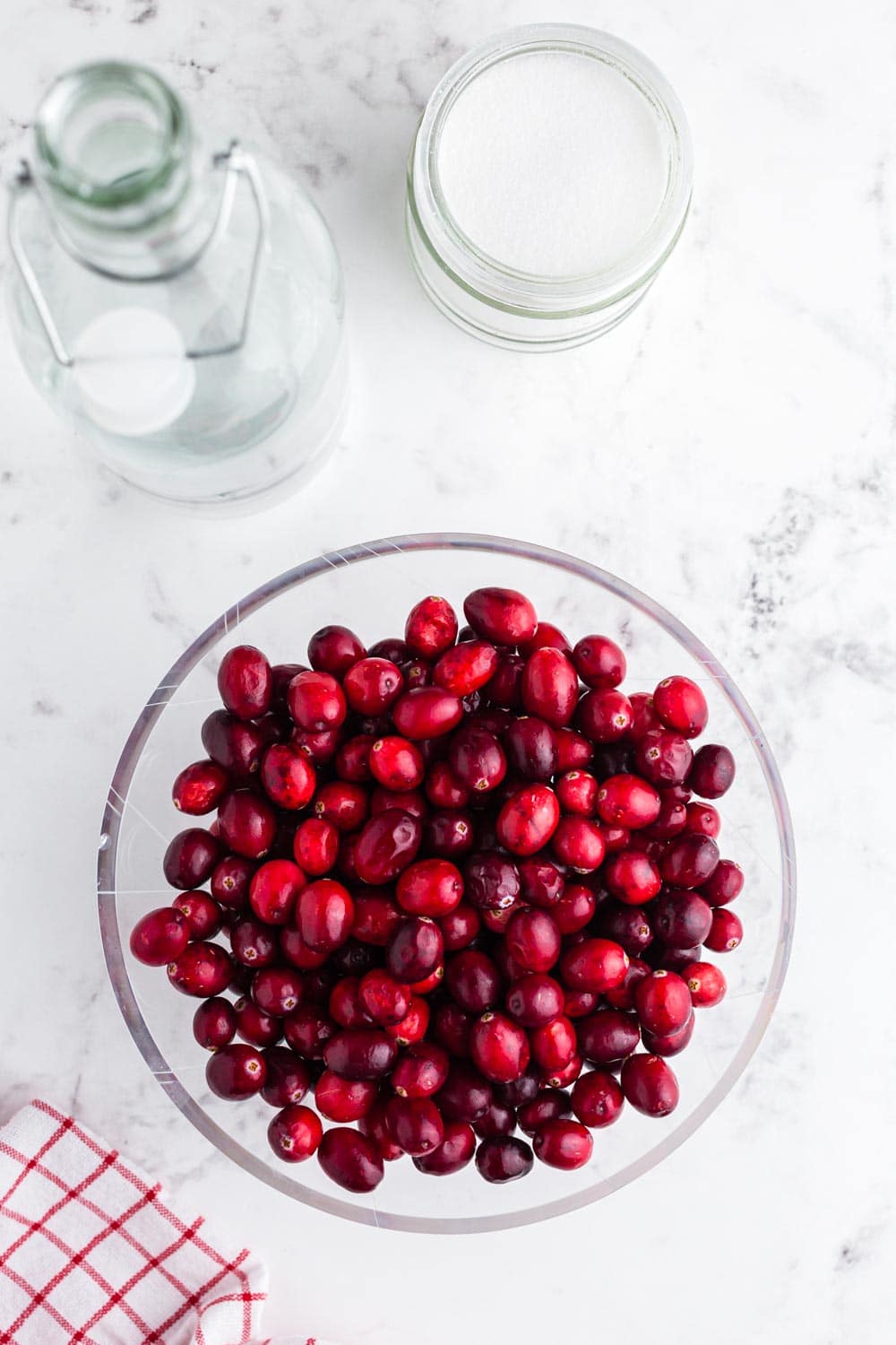 bowl of fresh cranberries, bowl of sugar, and bottle of water.