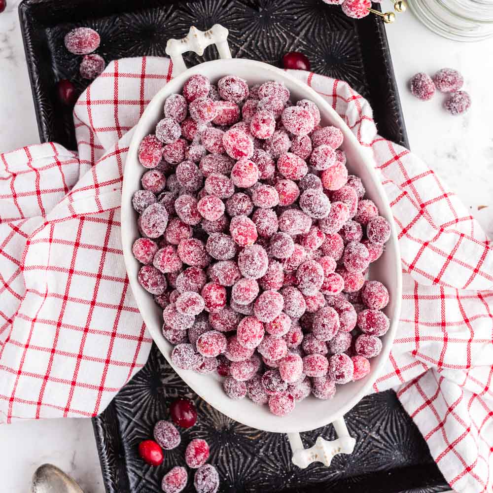 large white bowl filled with sugared cranberries on top of a red and white cloth.