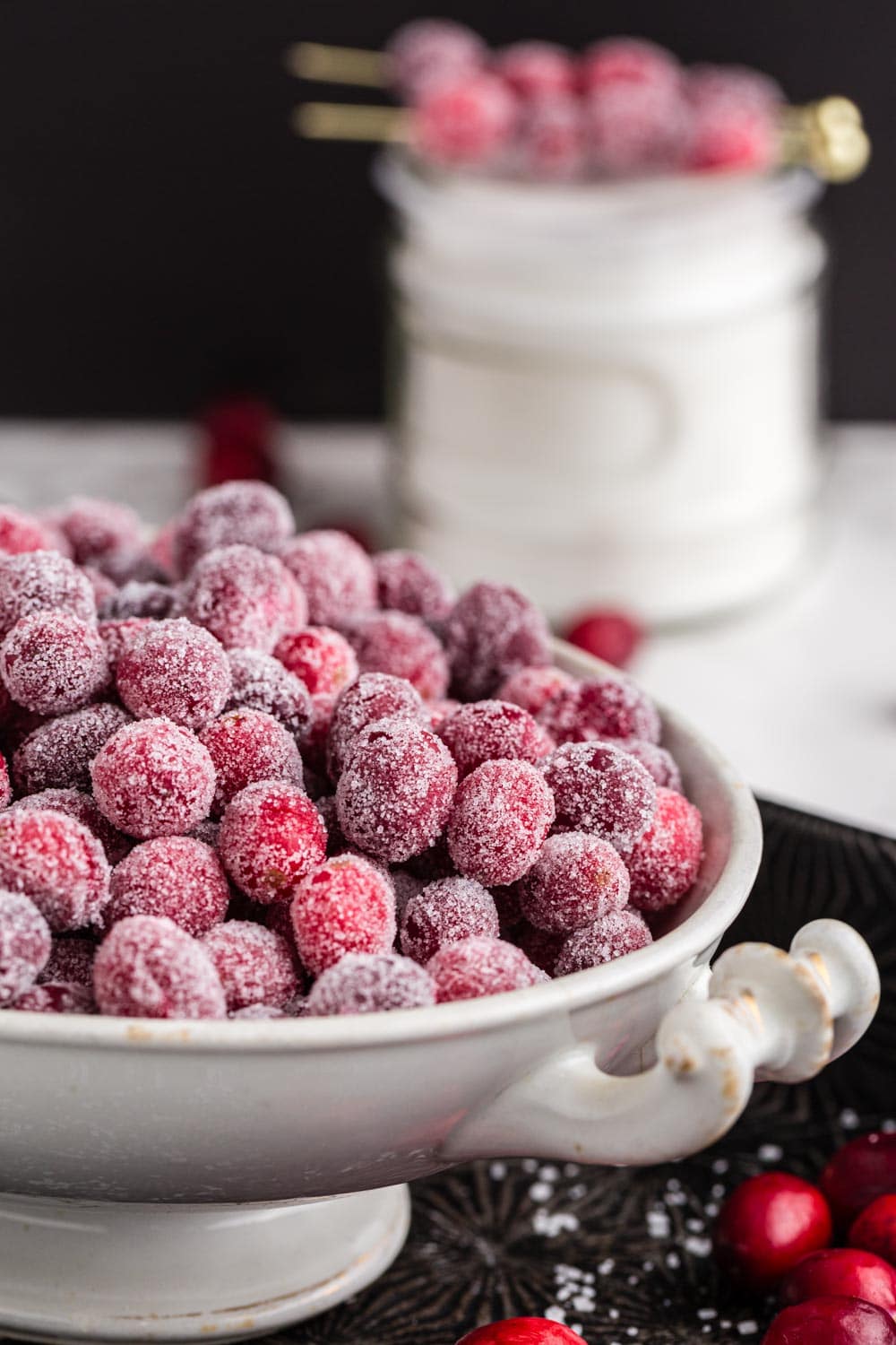 close up view of candied cranberries in a while platter with decor in the background.