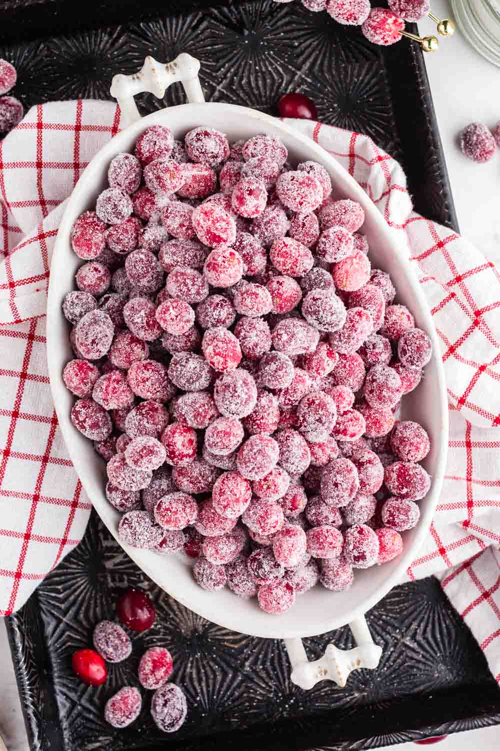 sugared cranberries in a large white bowl with white and red cloth placed underneath.