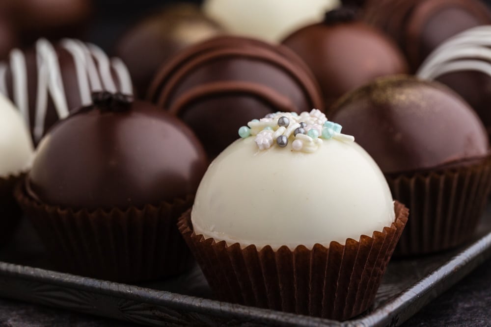 hot cocoa bombs in cupcake liners on a baking sheet decorated with piped chocolate and sprinkles