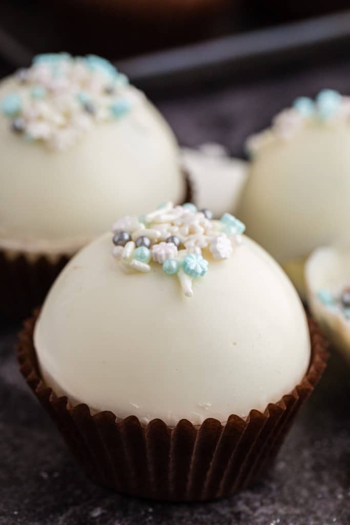 close up of white hot chocolate bombs topped with winter sprinkles in a cupcake liner