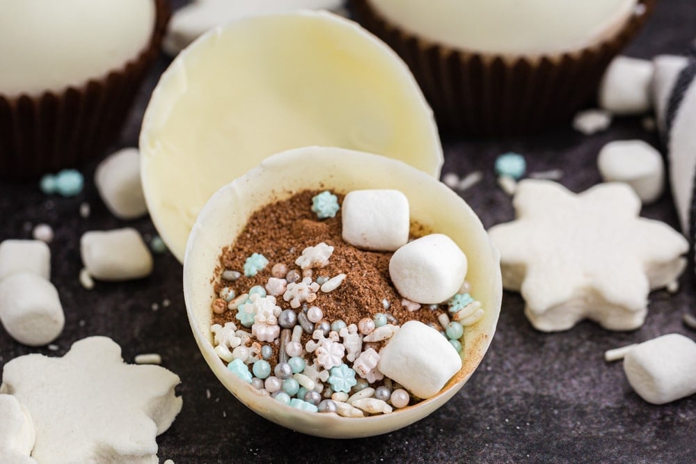 white chocolate cocoa bomb opened with chocolate powder, marshmallow, and sprinkles inside