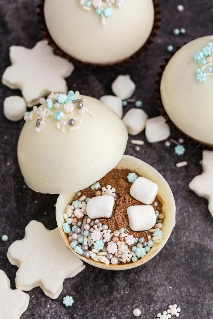 winter white hot chocolate bombs topped with sprinkles with one that is open showing cocoa and marshmallows