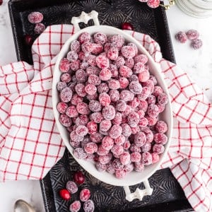 sugared cranberries in white oval serving dish on top of vintage cookie sheet with red and white linen