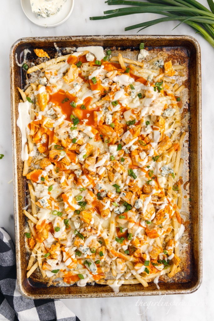 loaded buffalo chicken fries on a sheet pan next to green onions and blue cheese crumbles in a bowl