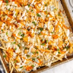 buffalo fries with chicken fresh out of the oven on a baking sheet topped with blue cheese crumbles