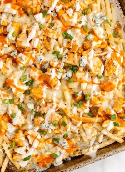 buffalo fries with chicken fresh out of the oven on a baking sheet topped with blue cheese crumbles