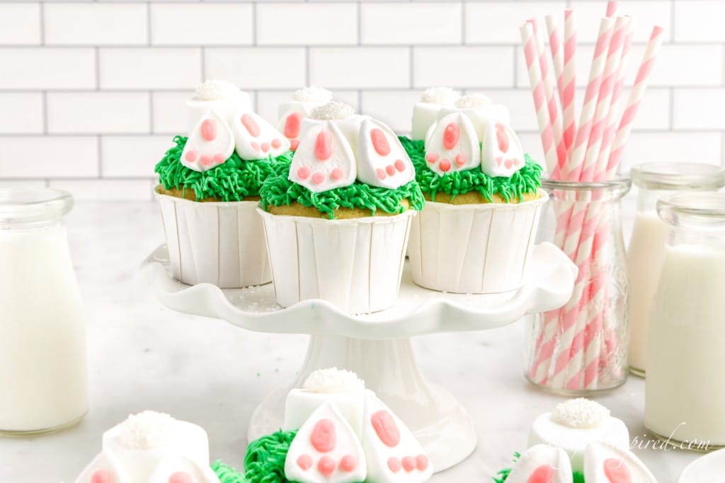 bunny butt cupcakes on a cake stand next to glasses of milk and pink paper straws