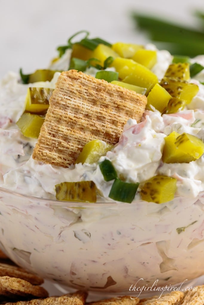 clear bowl filled with dill pickle dip, garnished with chopped pickles and Triscuit cracker